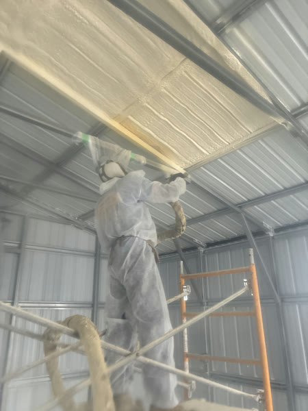 Technician on scaffolding spraying closed-cell foam insulation on a metal pole barn ceiling