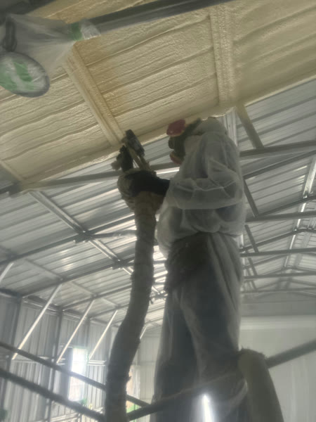 Close-up of a technician applying spray foam insulation overhead in a pole barn